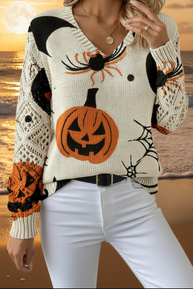 A woman wearing a cream-colored knit sweater with a Halloween pattern featuring orange pumpkins, black spiders, bats, and webs, paired with white pants.