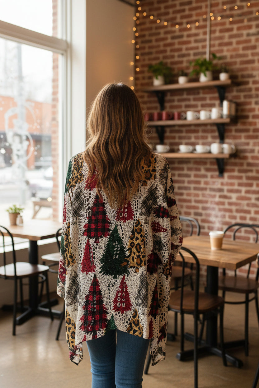 A close-up of a person wearing a loose, off-white knit top with a multicolor Christmas tree pattern, including red, green, and plaid tree motifs. In coffee shop,