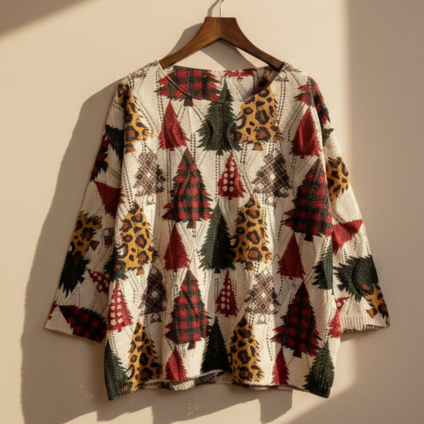 A long-sleeve knit top with a festive Christmas tree pattern, hanging on a wooden hanger against a white background. The pattern features red, green, black, and brown trees on an off-white base.