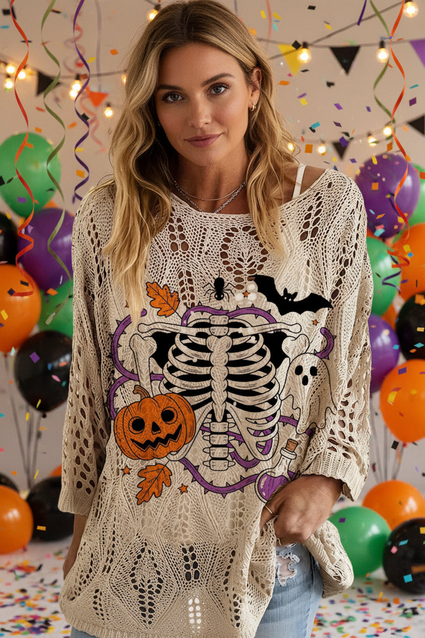 A woman wearing a cream-colored open-knit sweater with a large Halloween graphic on the front, featuring a black skeleton, orange jack-o'-lantern, purple skull, and bats.