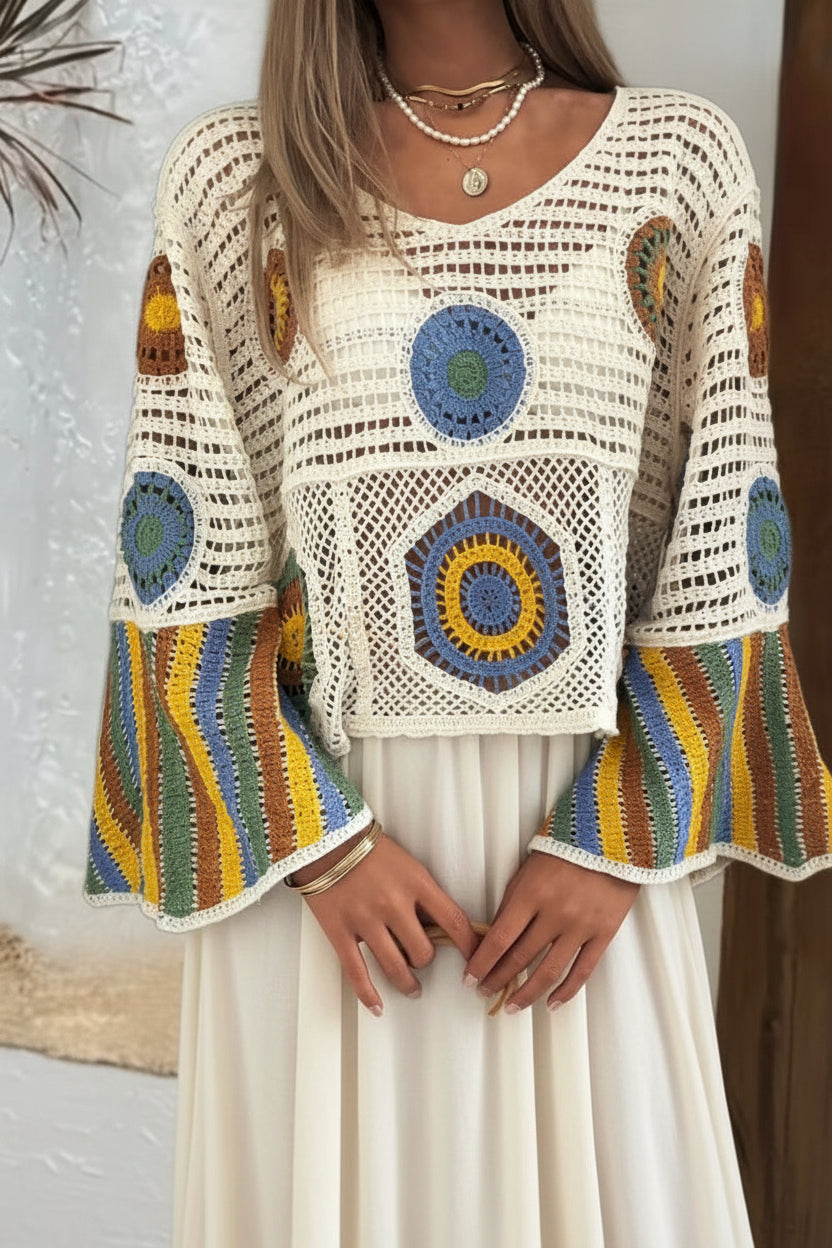 A woman wearing a cream crochet knit top with colorful circular and striped crochet details, paired with light-wash denim shorts.