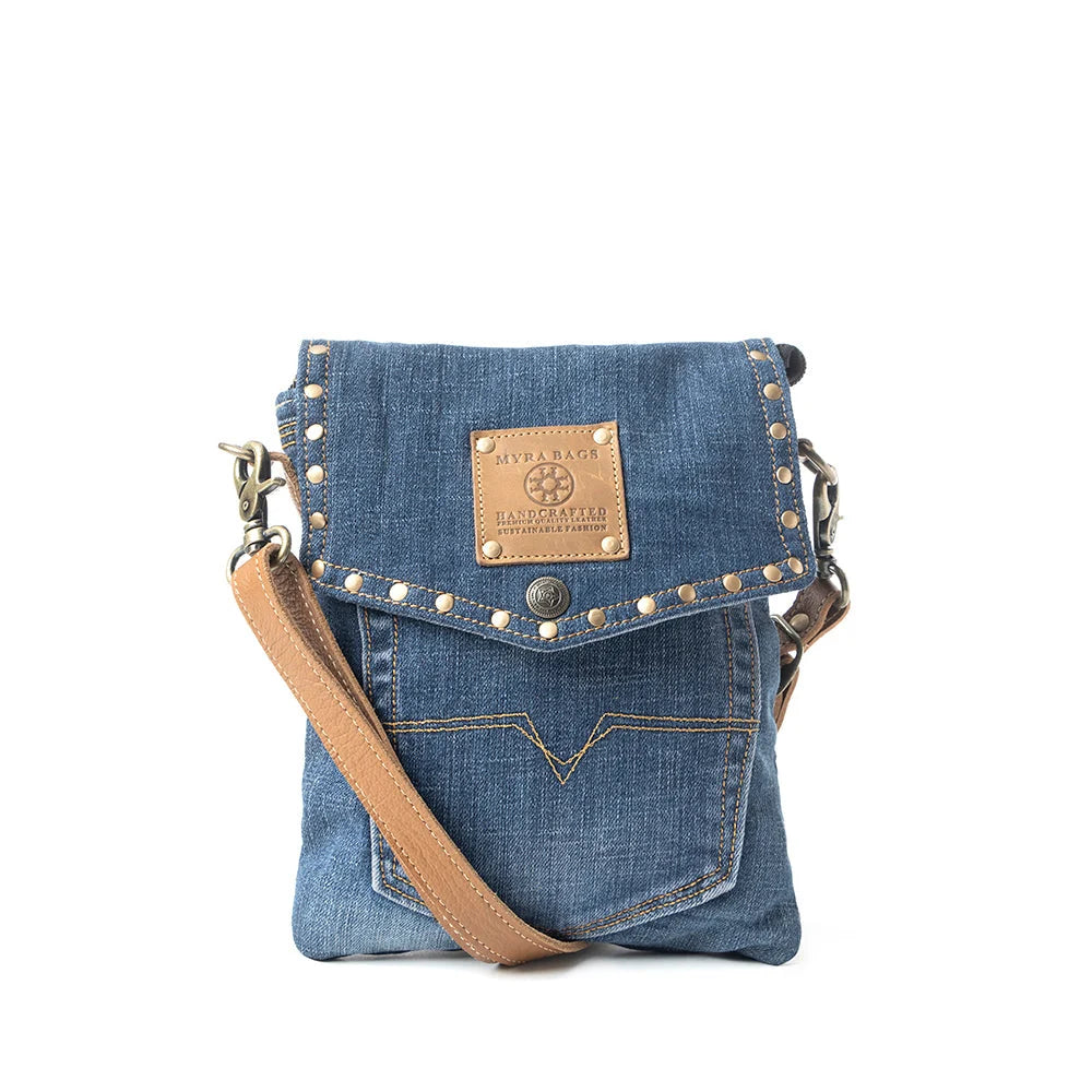 Myra Dahlia Denim Crossbody Bag with blue upcycled denim, brass stud accents, leather flap detail, and shoulder strap across the front