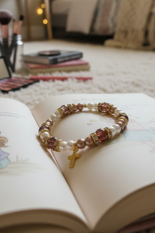 Handmade pearl and pink beaded stretch bracelet with gold cross charm displayed on an open book