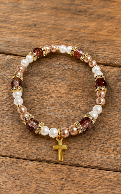 Handmade stretch bracelet with white and blush pearl accents, brown glass beads, gold-tone spacers, and gold cross charm on rustic wood