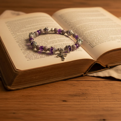 Purple and lavender beaded stretch bracelet with silver cross charm displayed on an open book